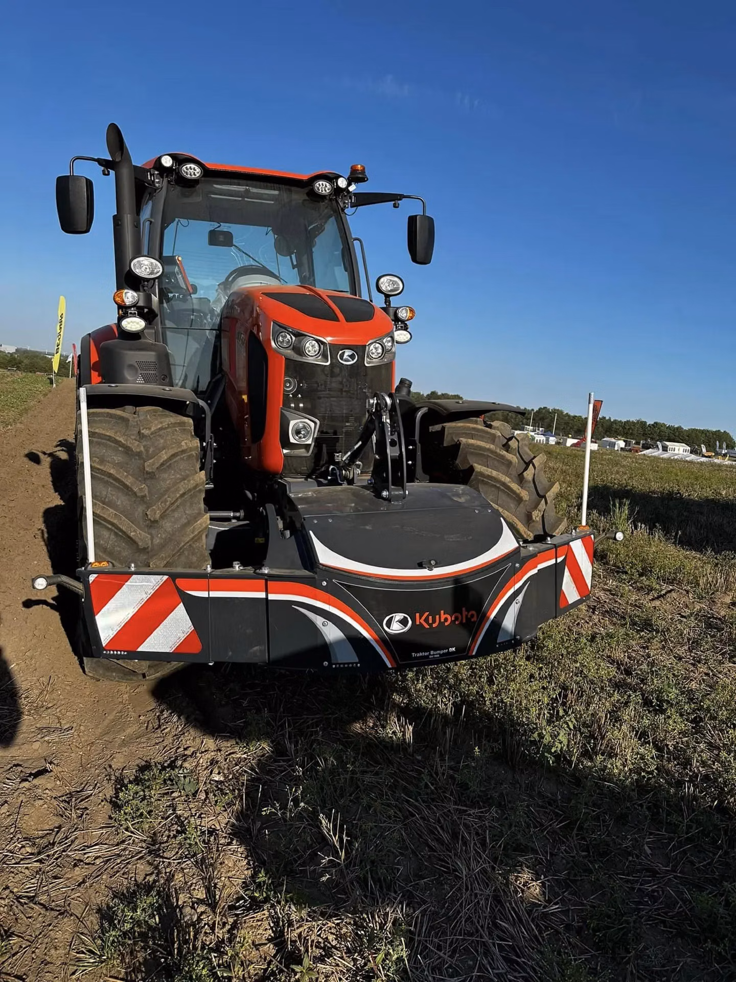 A red tractor fitted with a Kubota branded front weight bumper featuring reflective safety markings