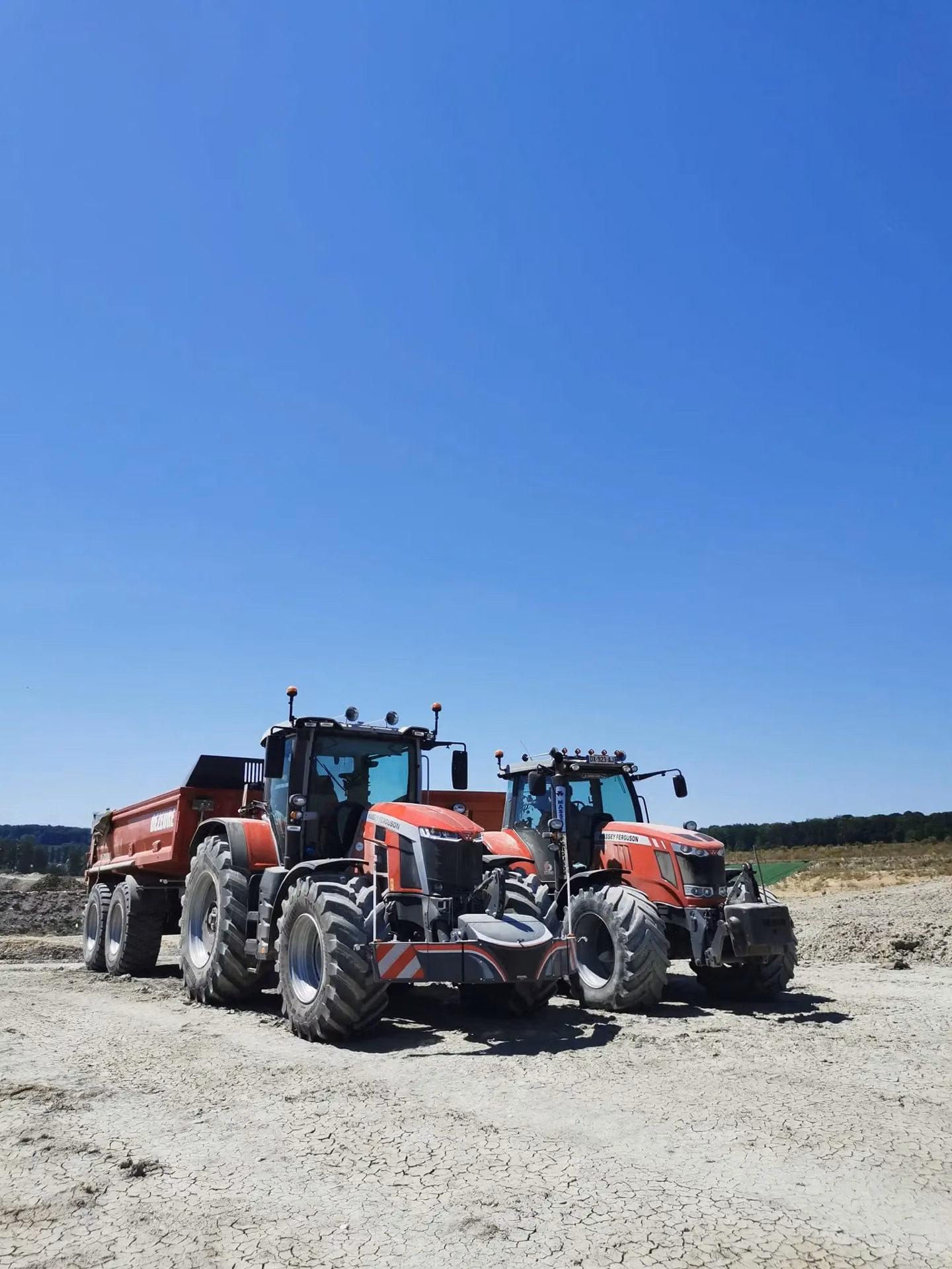Two red tractors with front weight bumpers parked on dry, cracked soil under a clear blue sky