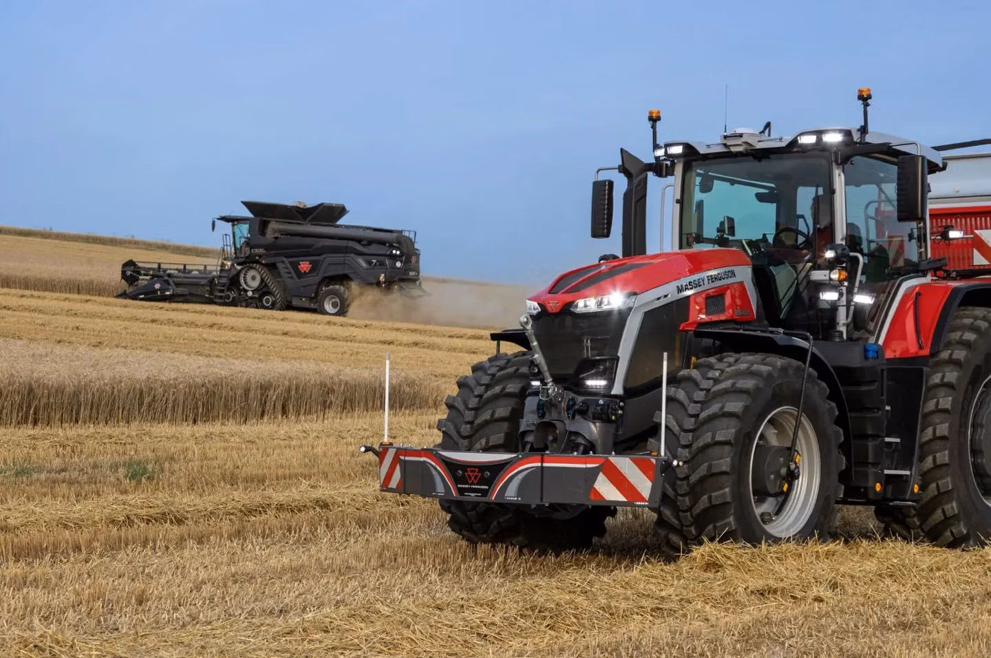 A Massey Ferguson tractor with front weight bumper in a harvested field, combine harvester in the background