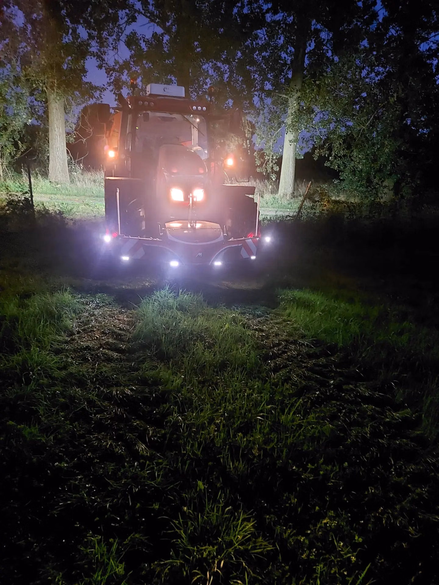 A tractor at night on grass with a front weight bumper featuring multiple bright LED lights illuminated