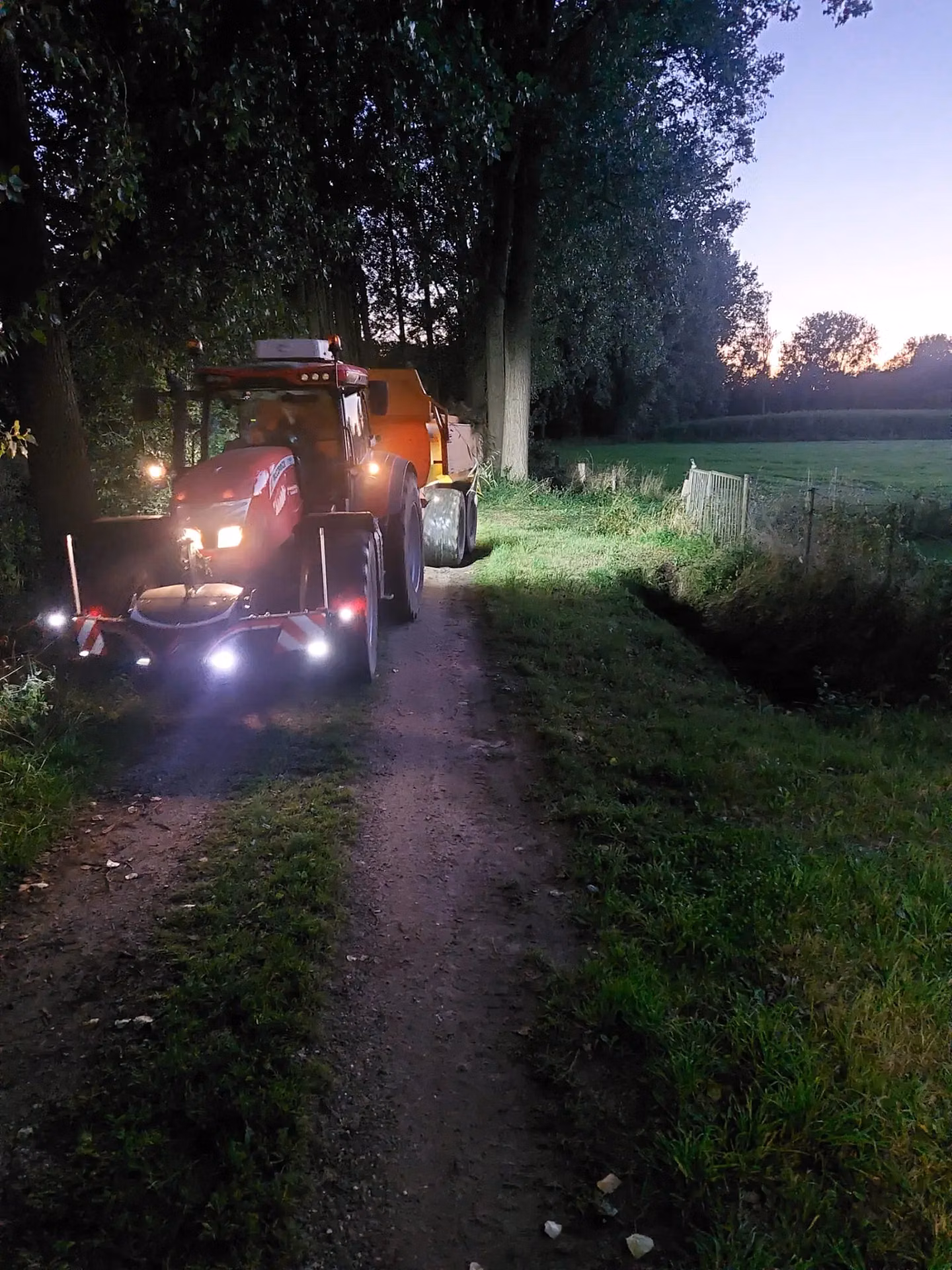 Red tractor with a front weight bumper featuring LED lights is parked on a rural dirt path at dusk