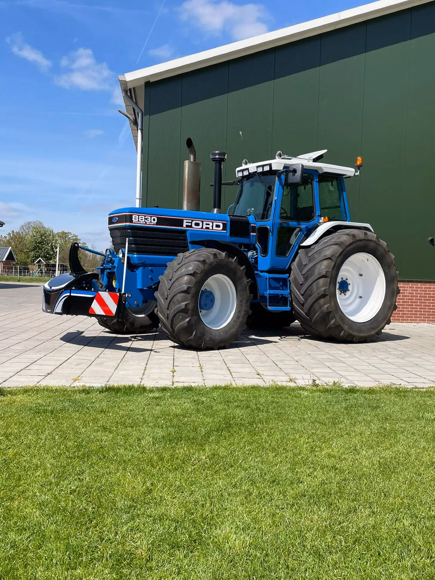 Blue tractor with large rear tires and a black front weight bumper with red and white safety stripes attached