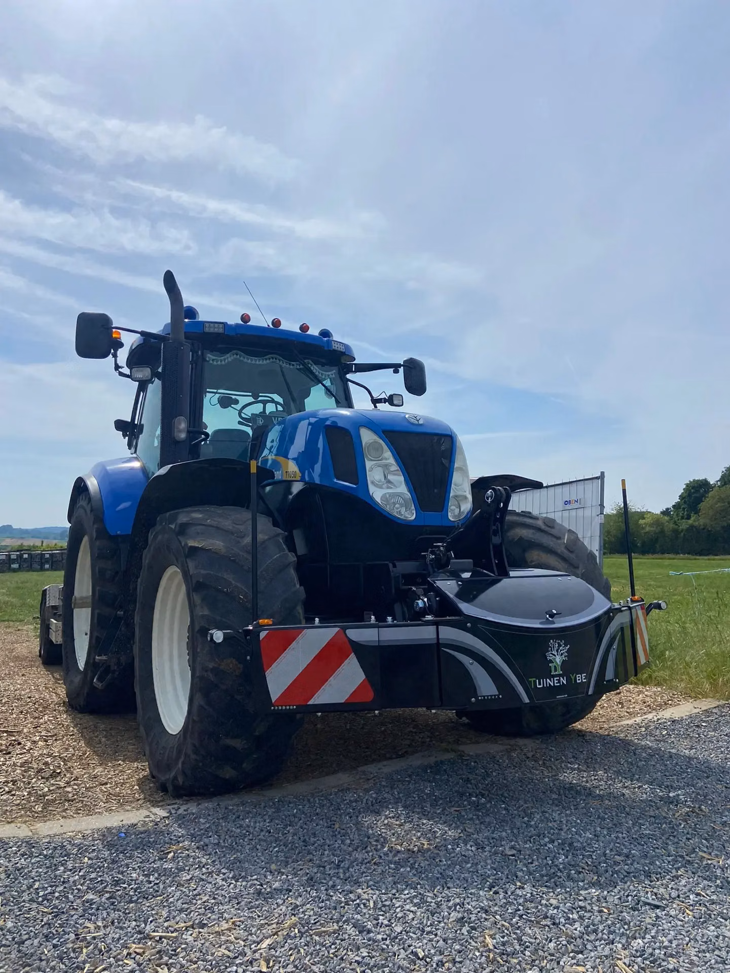 Blue tractor with large tires fitted with a front weight bumper featuring LED lights and red and white safety stripes