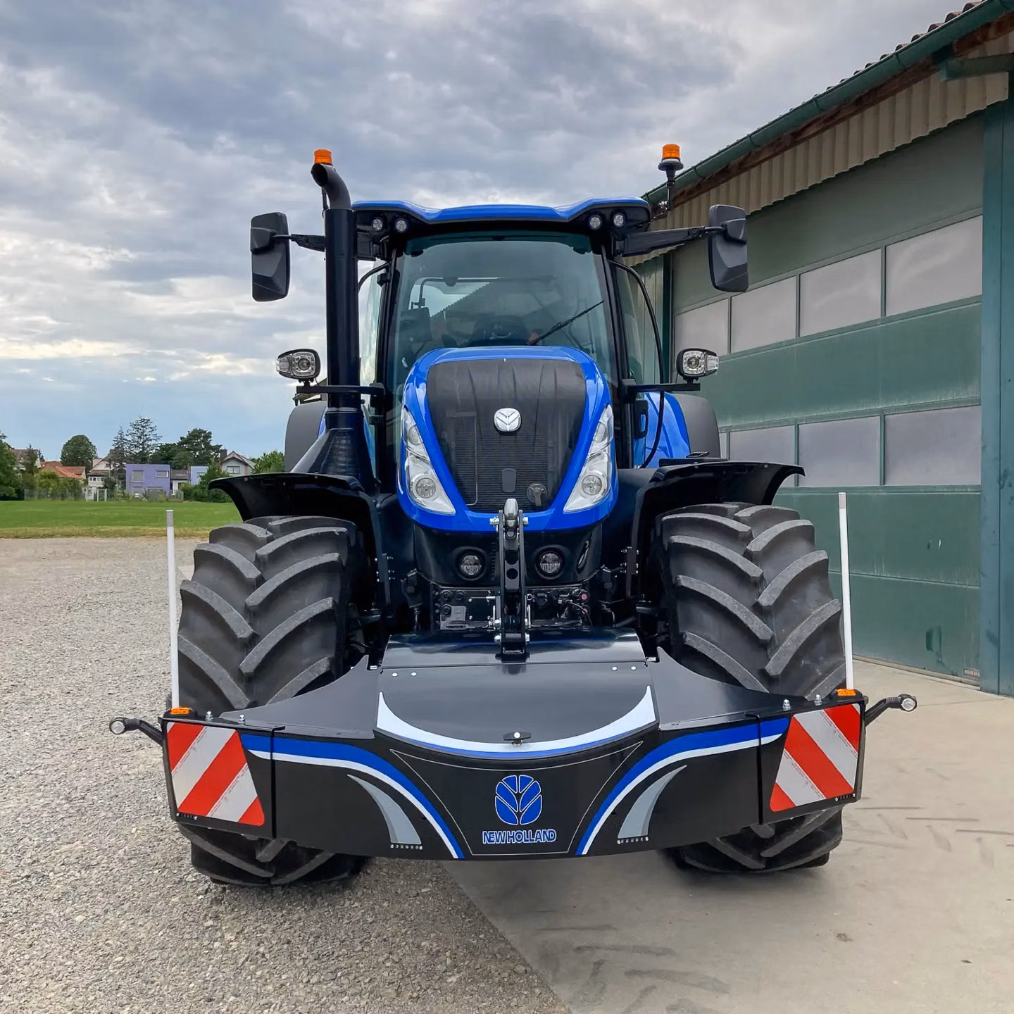 Blue tractor with a front weight bumper displaying the New Holland logo and red-white warning stripes