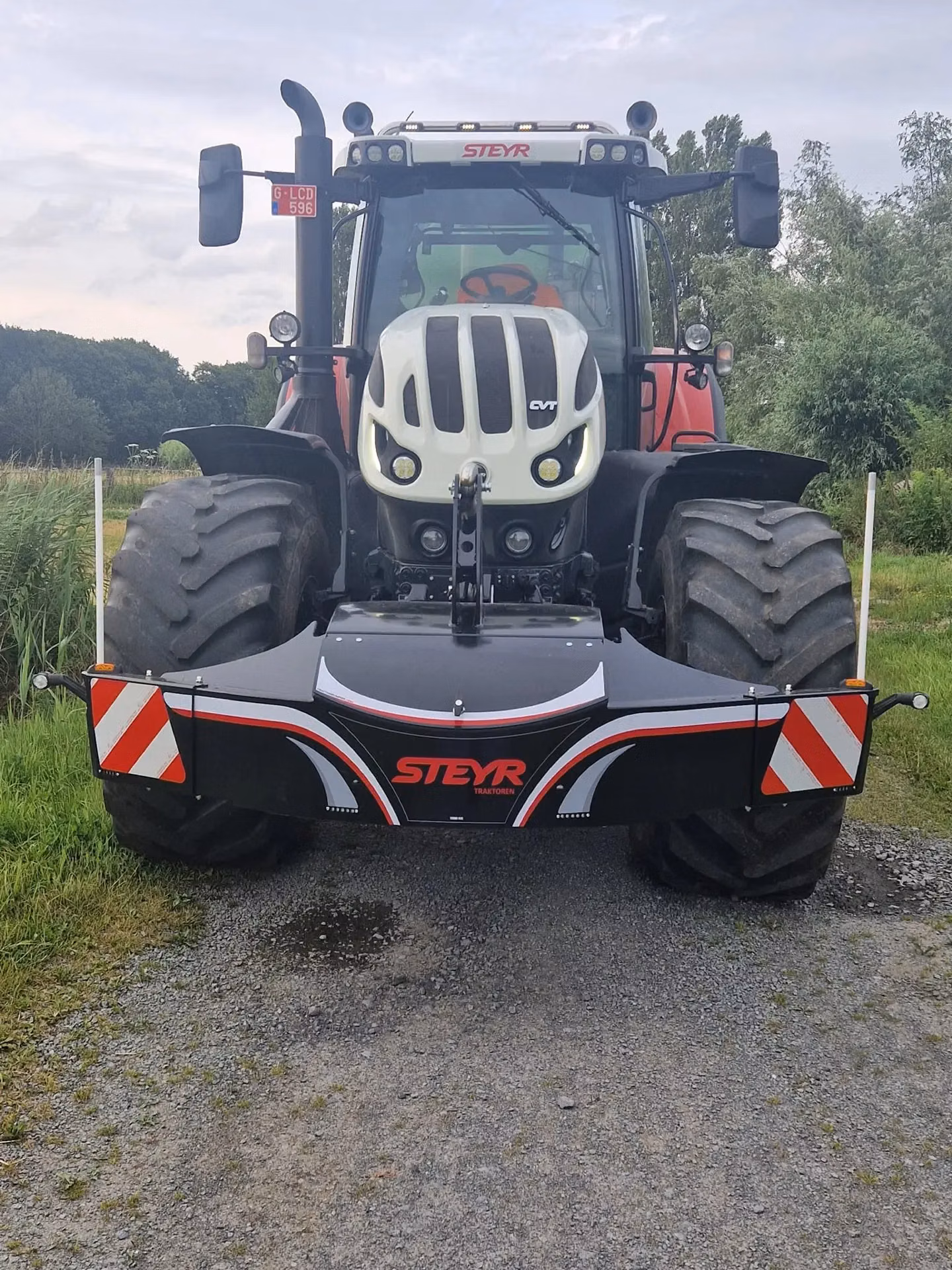 Tractor on a gravel path with a large front weight bumper featuring red and white stripes and STEYR branding