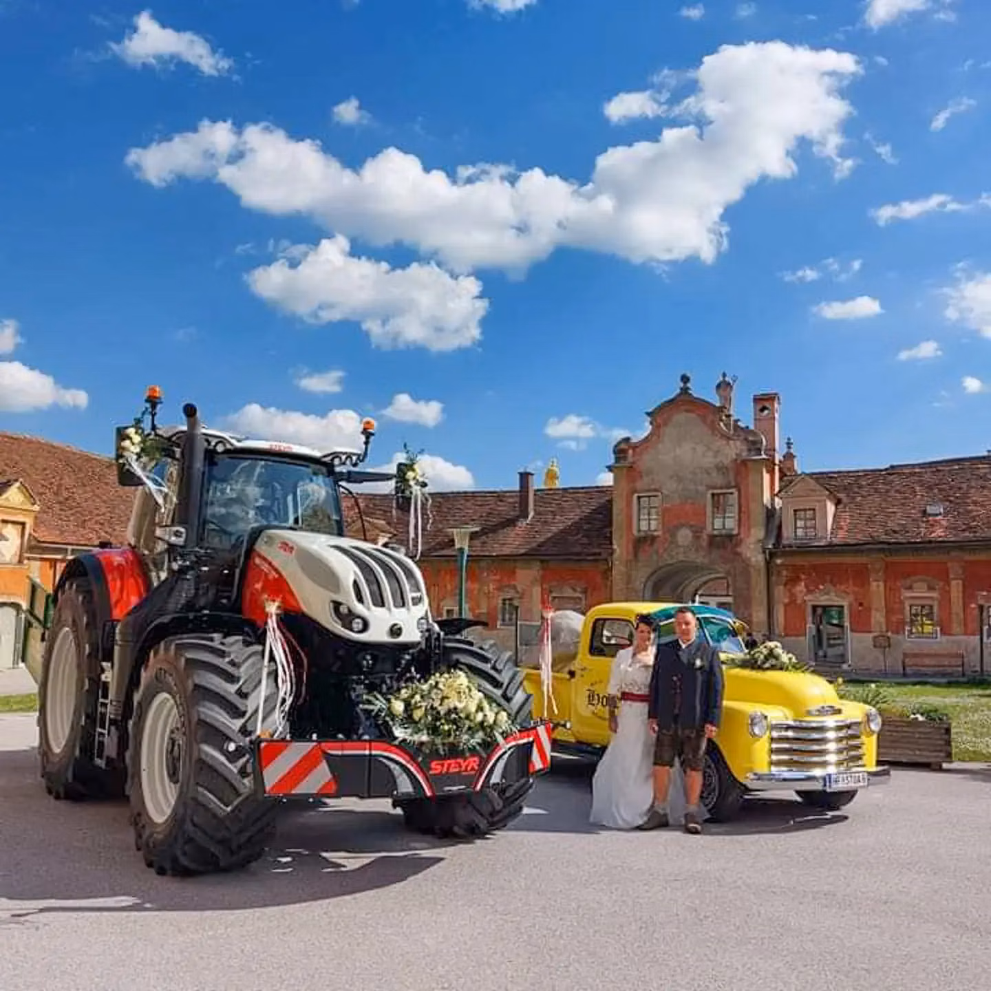 Tractor with a front weight bumper decorated with flowers and ribbons parked next to a classic yellow car and two people