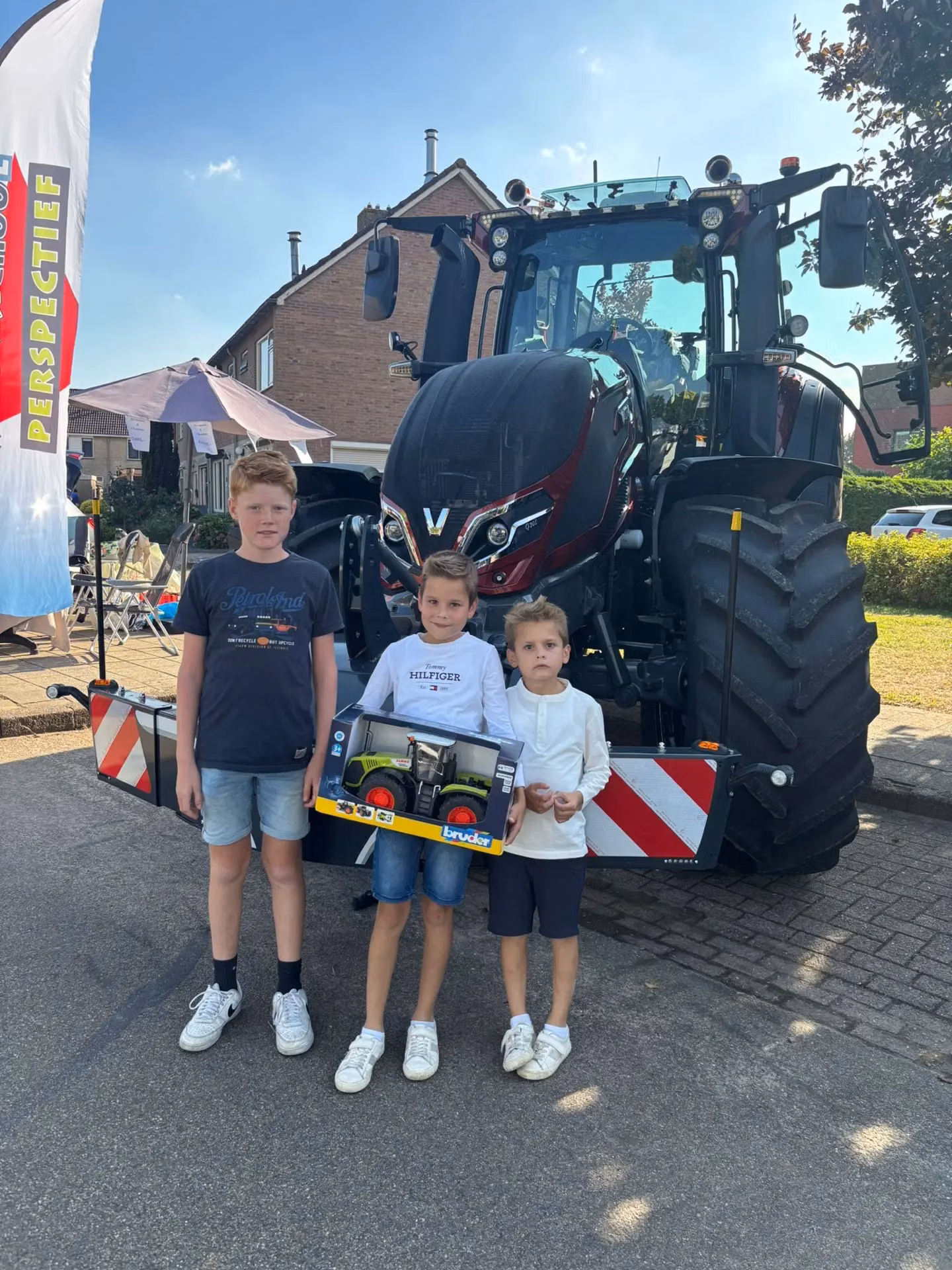 Three children stand in front of a tractor fitted with a front weight bumper with red and white safety stripes