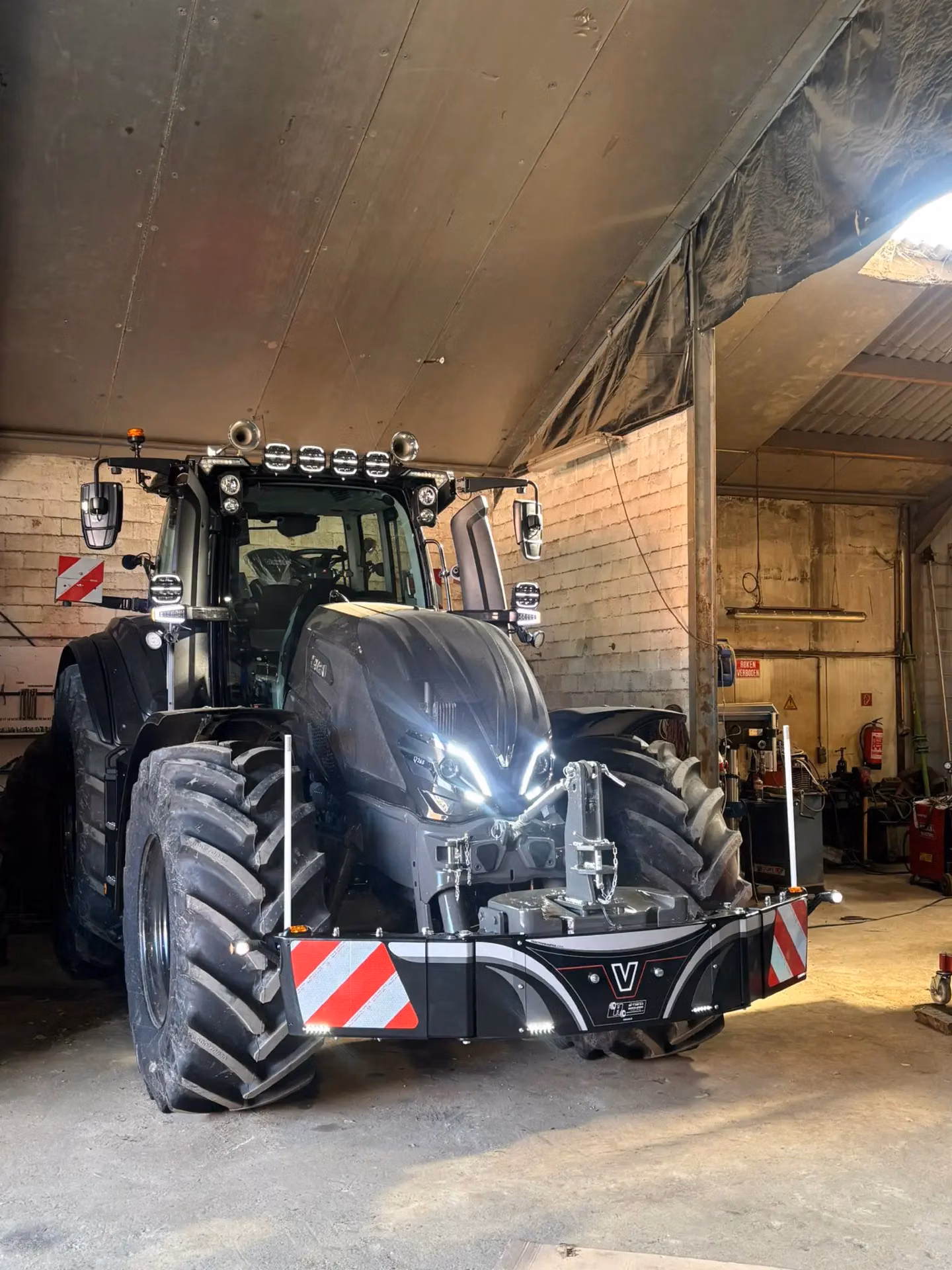 A large black tractor with a front weight bumper featuring LED lights and red-white safety stripes in a workshop.