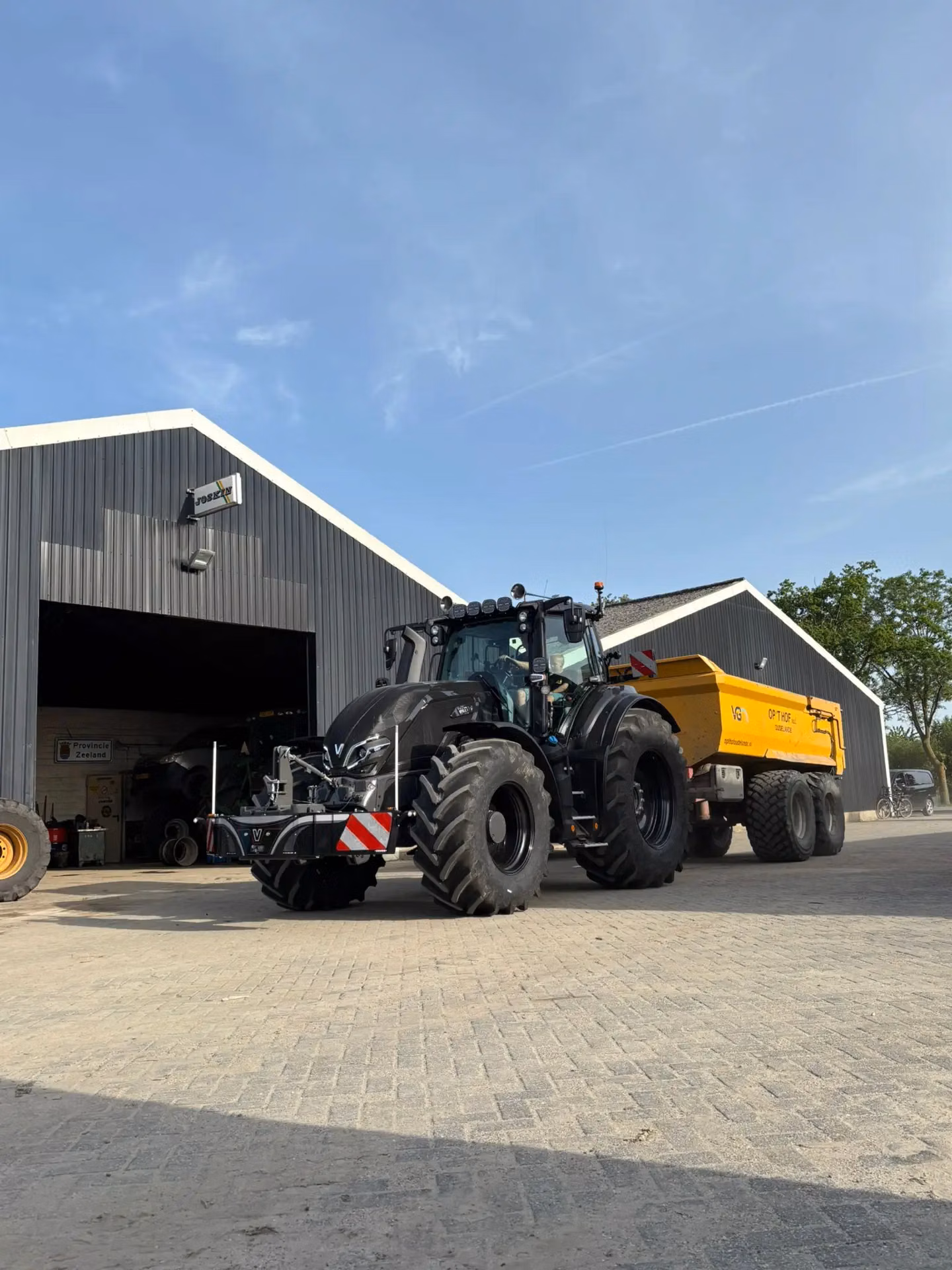 Black tractor fitted with a front weight bumper featuring LED lights and storage, parked on a paved surface near farm