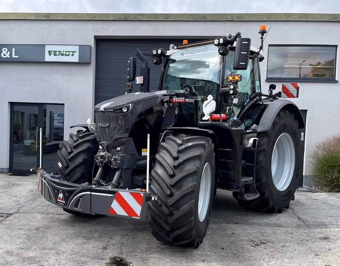 A large black tractor with a front weight bumper attached, parked on concrete in front of a building.