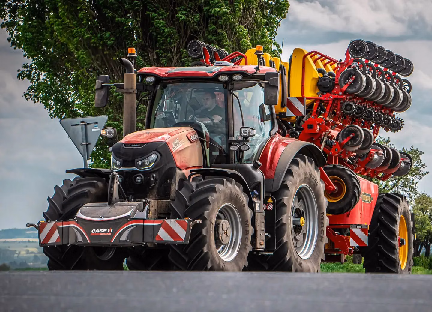 Red tractor with large front weight bumper and agricultural machinery attached on a rural road