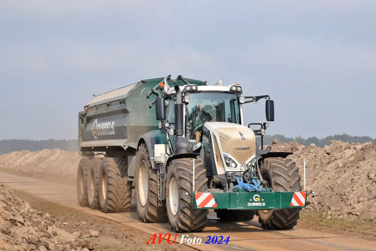 Green front tractor weight with LED lights and red-white safety stripes mounted on a large tractor on a dirt road