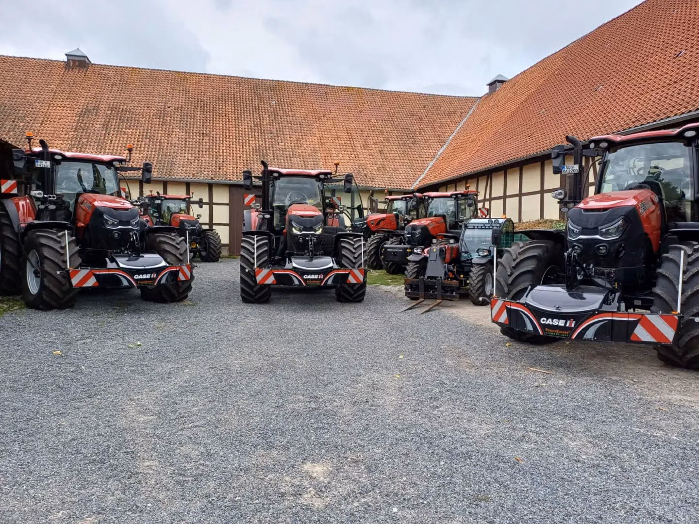 Five red tractors with front weight bumpers featuring reflective red and white stripes are parked in a farmyard.
