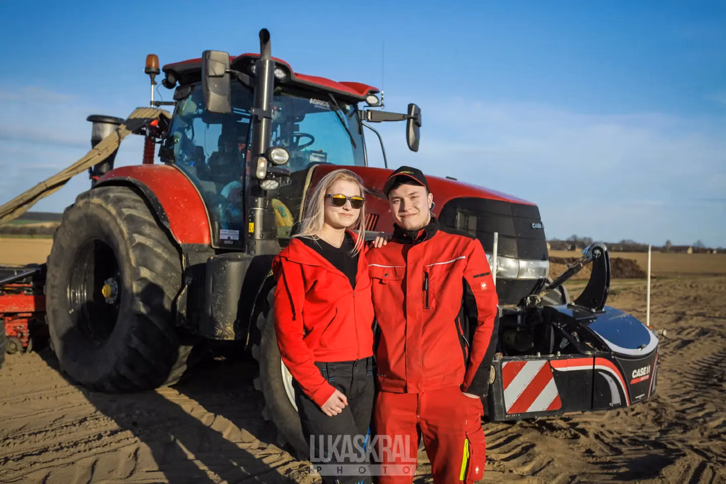 Two people in red workwear stand in front of a red tractor with a Case IH front weight bumper attached