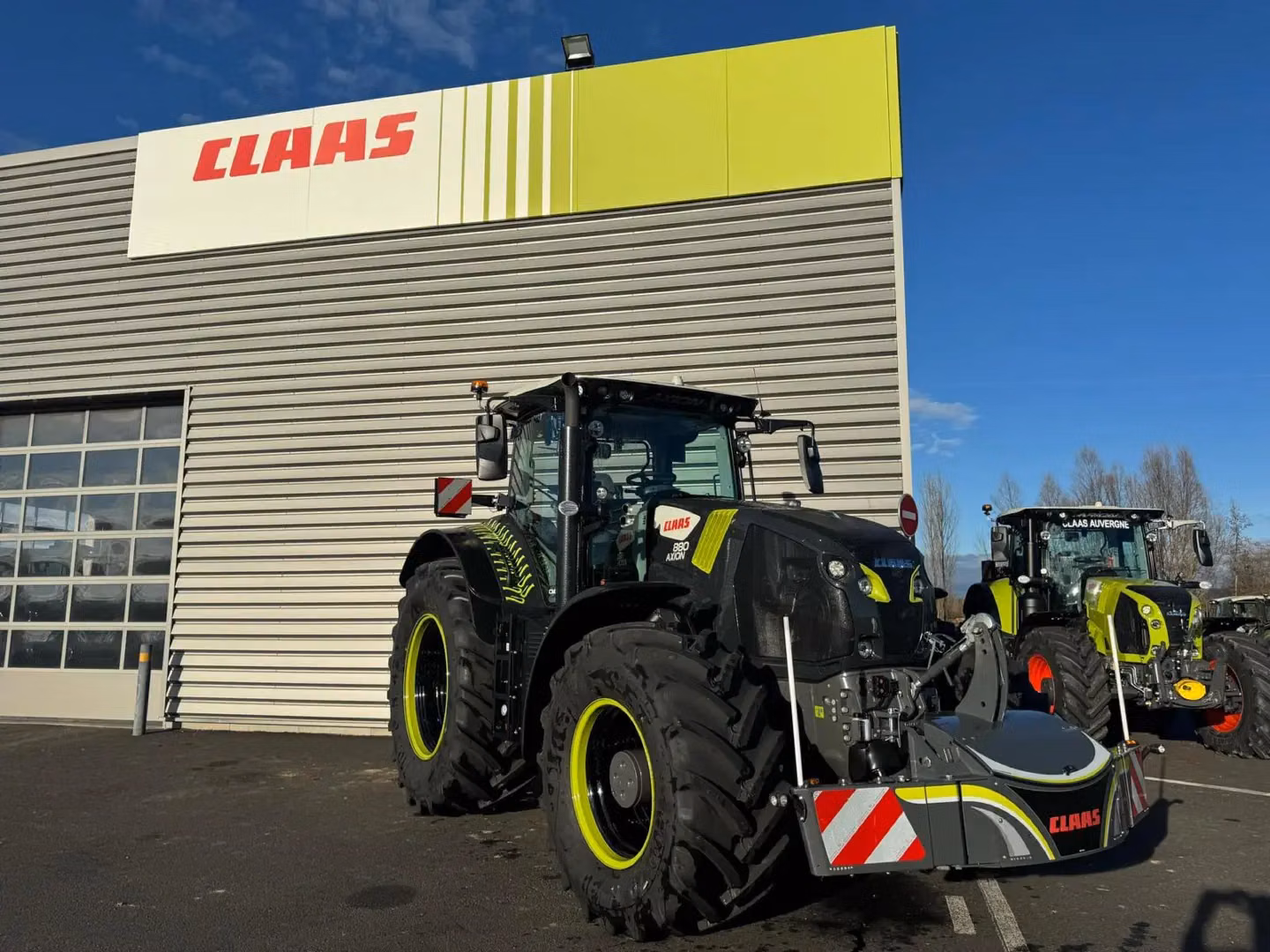 Two large tractors with yellow wheel rims and front weight bumpers are parked outside a building with a CLAAS sign