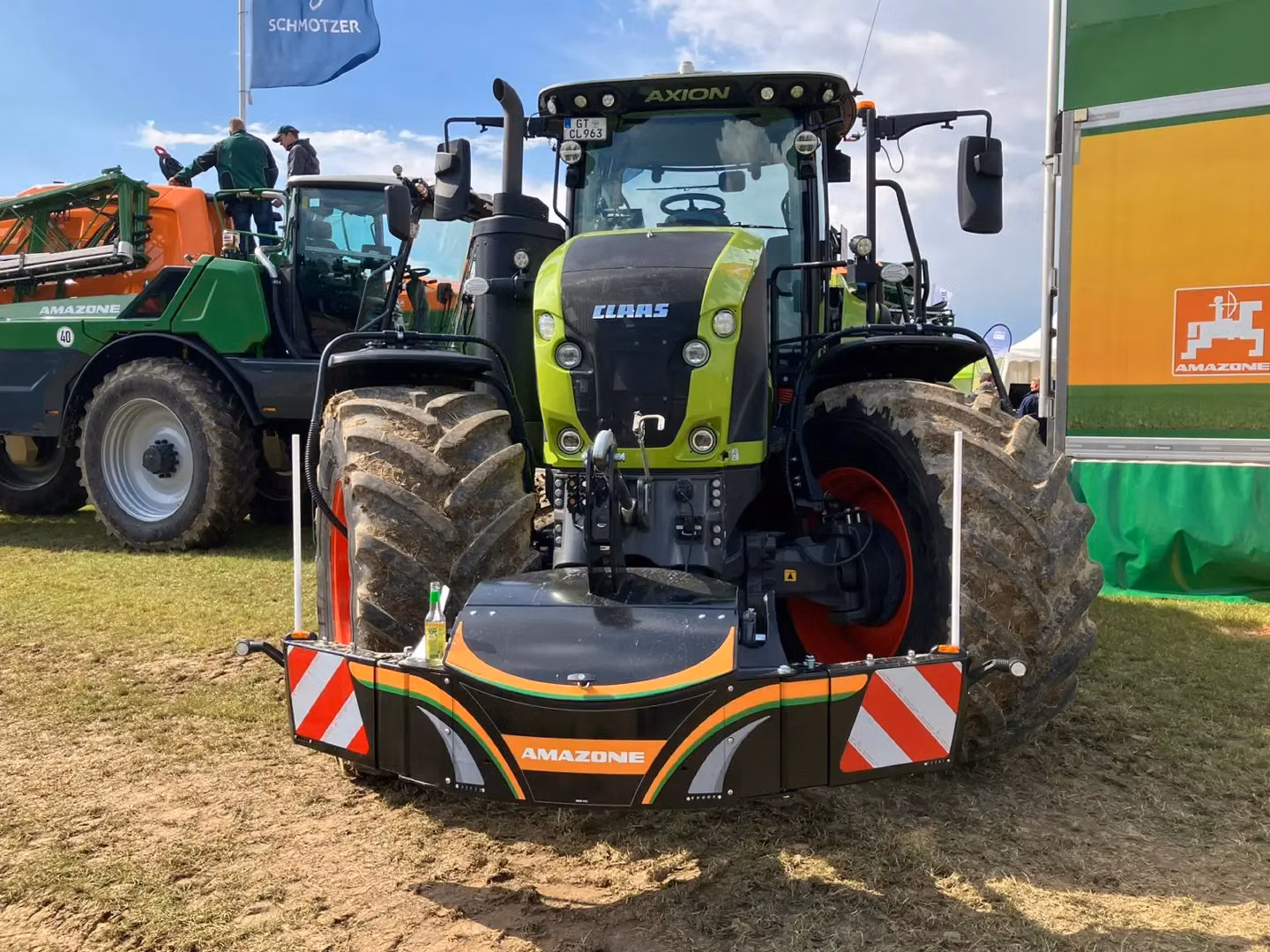 A green tractor with large muddy tires displays an attached front weight bumper marked with orange and white stripes