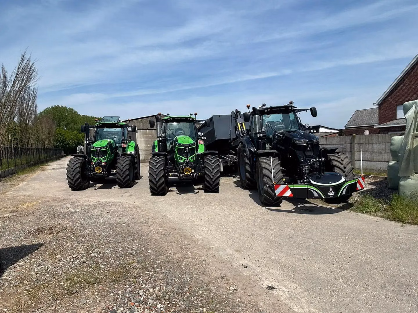 Three tractors are parked on a paved farmyard, the right one fitted with a large front weight bumper with reflectors