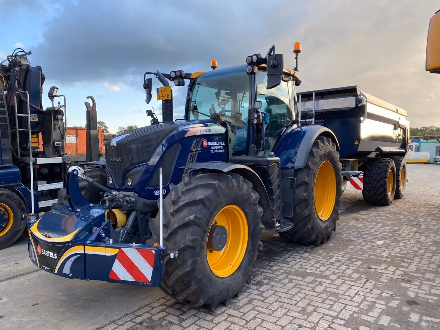 Dark blue tractor with yellow wheels and a trailer, fitted with a customized front weight bumper with reflective stripes