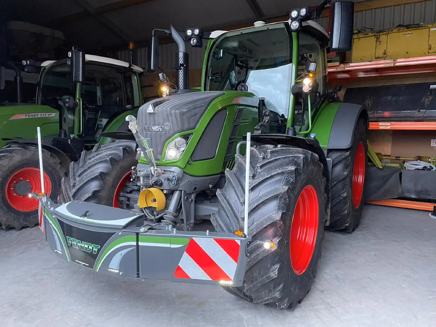 Green tractor with red wheels in a shed, fitted with a front weight bumper featuring reflectors and Fendt branding