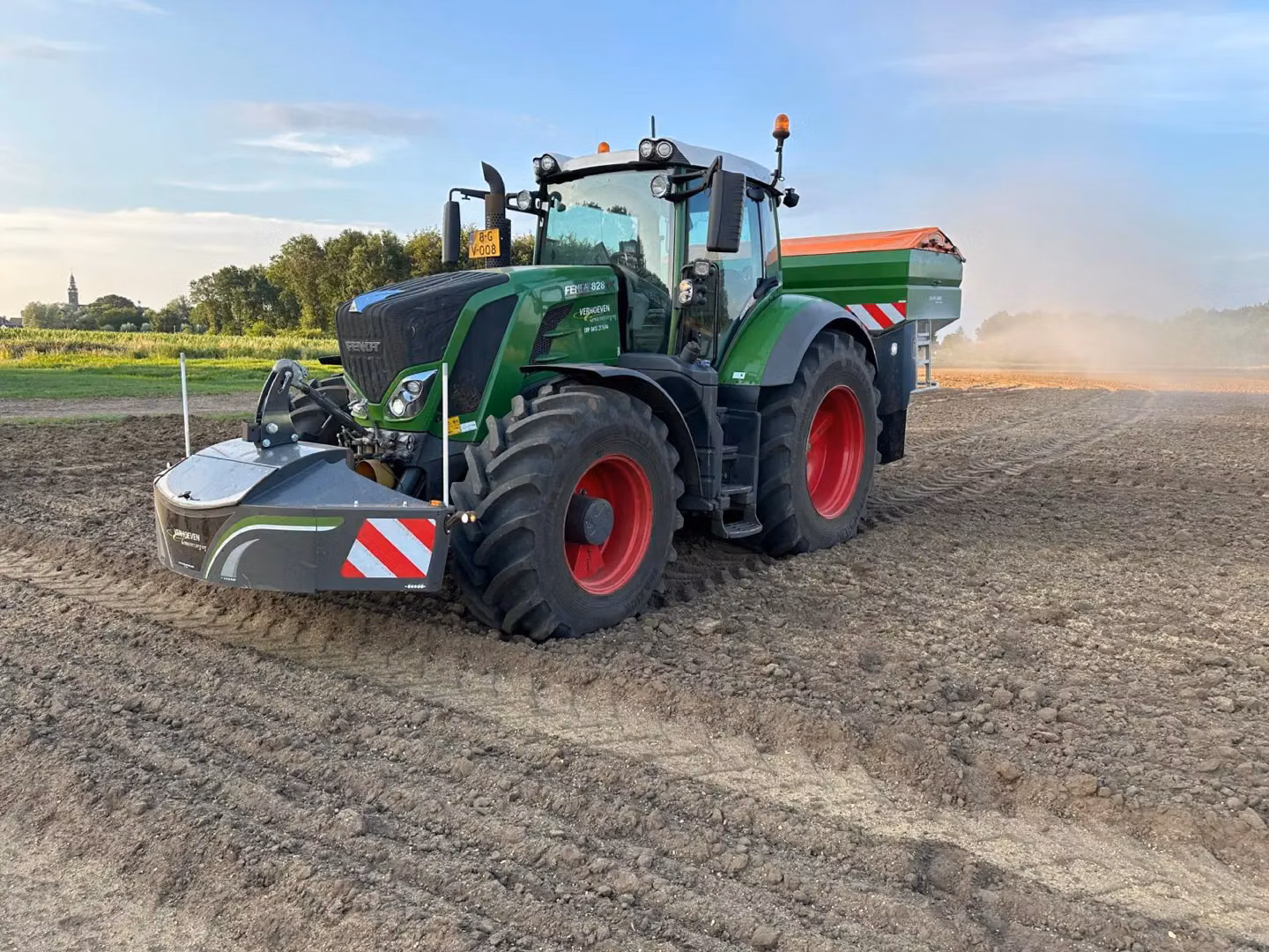 Green tractor with red wheels in a field, fitted with a front weight bumper featuring safety stripes and lights
