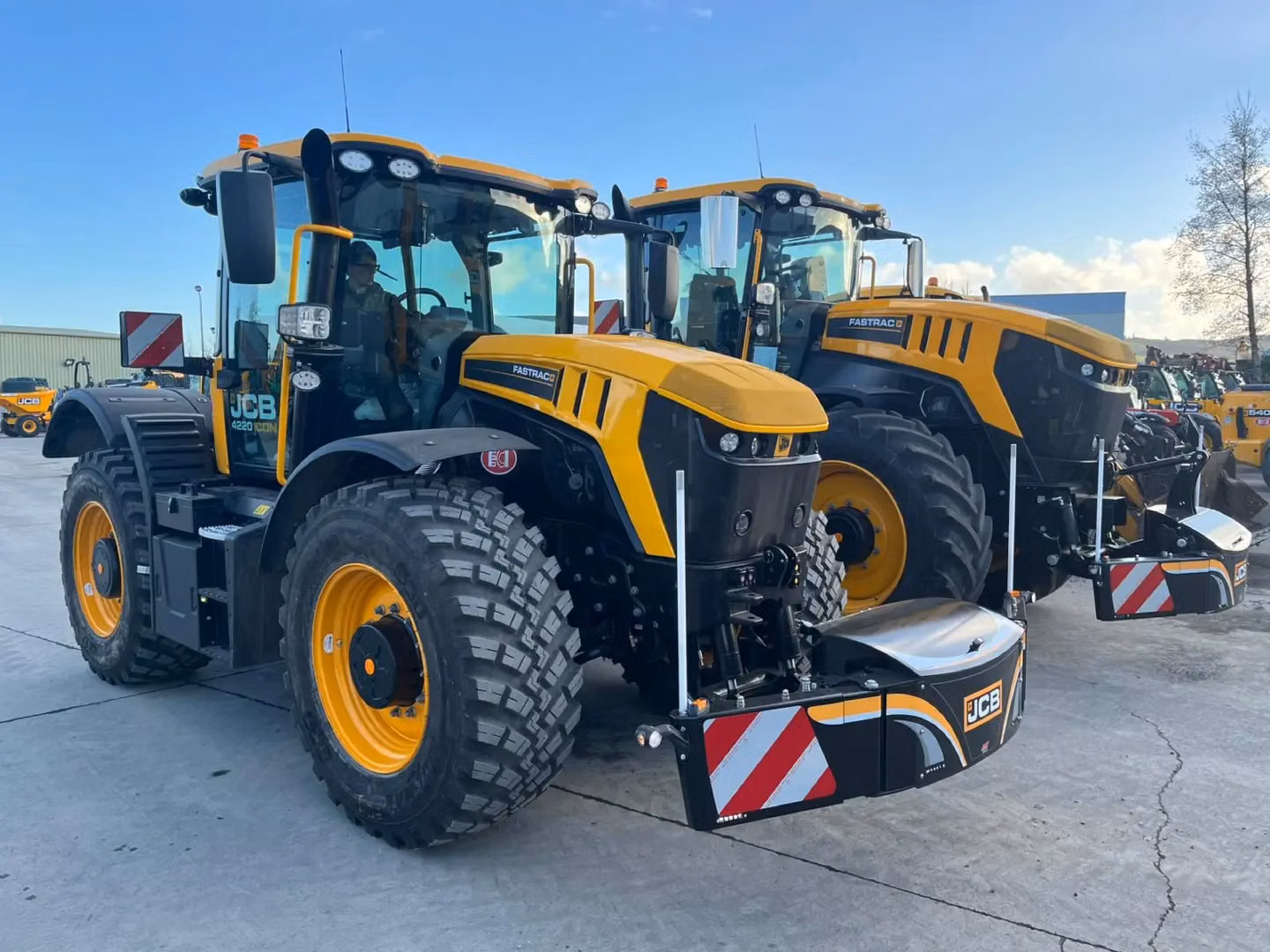 Two yellow tractors fitted with black and silver front weight bumpers with red and white safety stripes