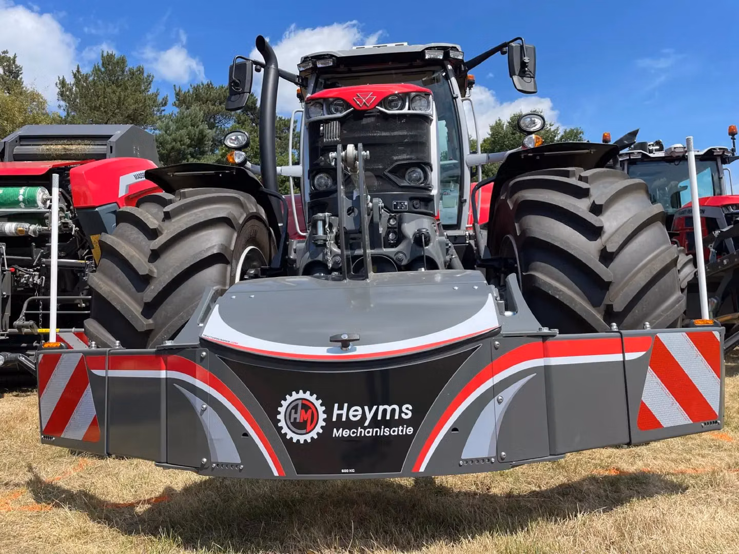 Large grey front weight bumper with red and white stripes mounted on a red tractor, with tractors in the background