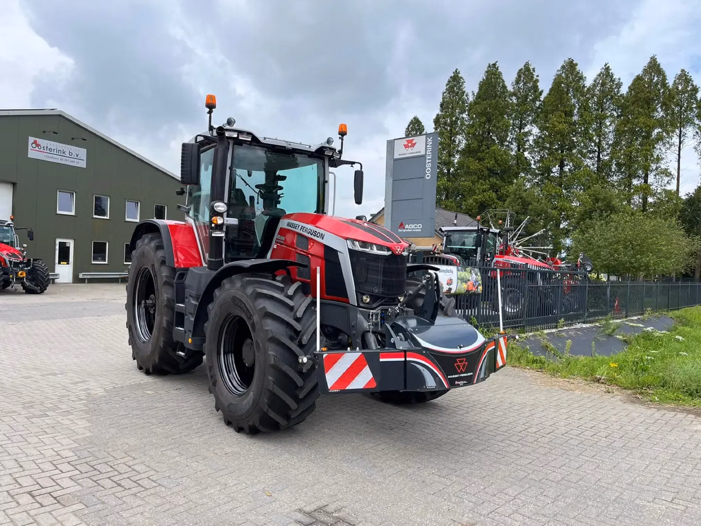 Red Massey Ferguson tractor with a front weight bumper featuring lights and reflective stripes, parked outside a building