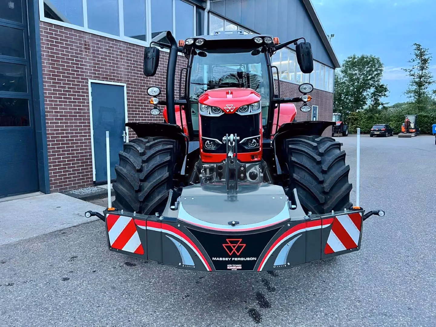 Red tractor fitted with a Massey Ferguson branded front weight bumper featuring reflective safety markings