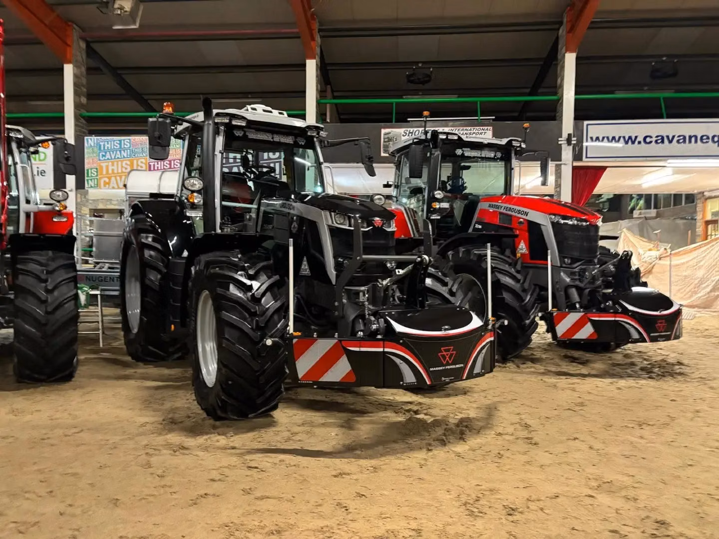 Two Massey Ferguson tractors equipped with front weight bumpers and LED cargo boxes are displayed indoors on sand