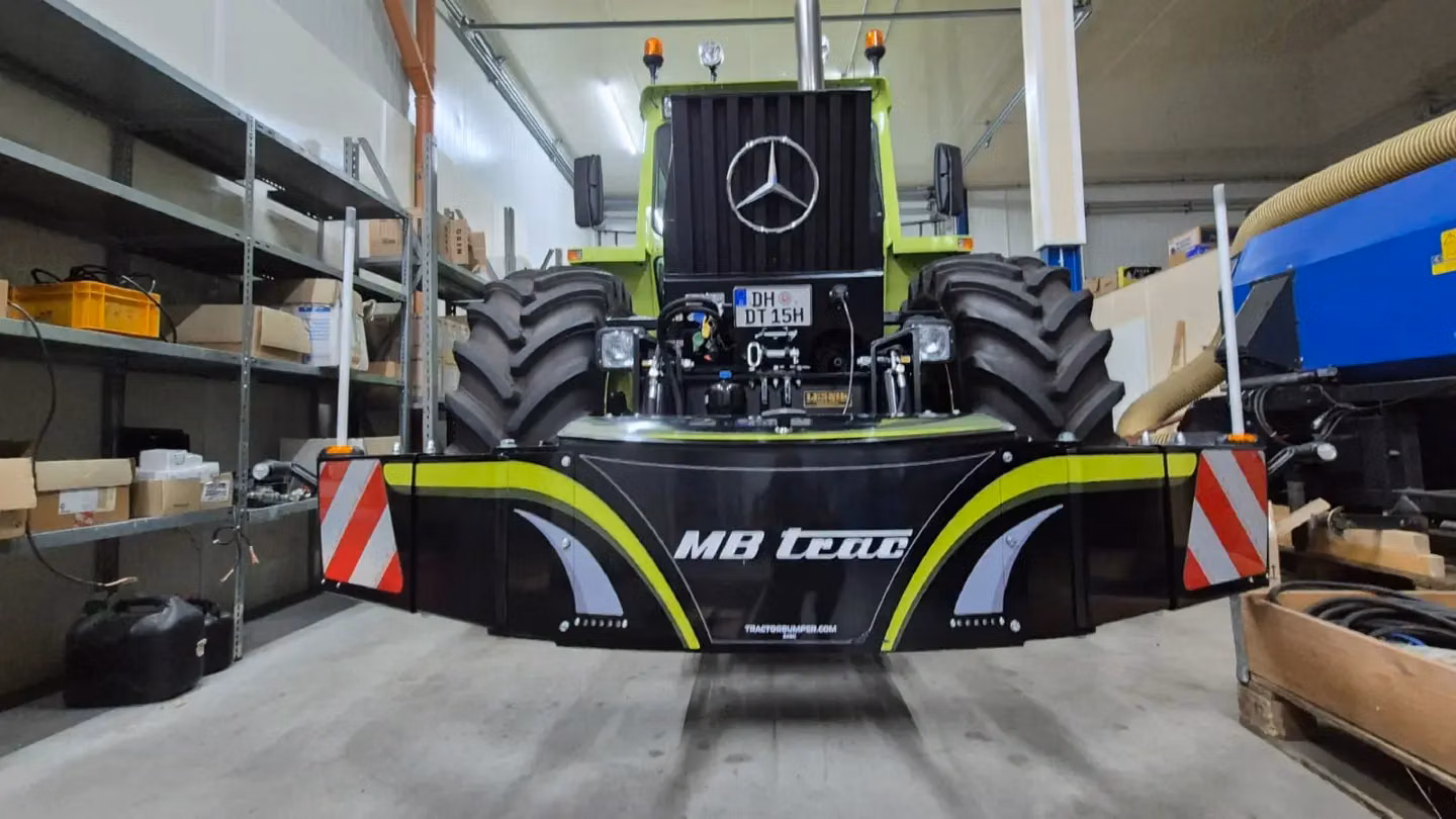 Front view of a tractor indoors with a large black front weight bumper labeled MB trac and red-white warning stripes