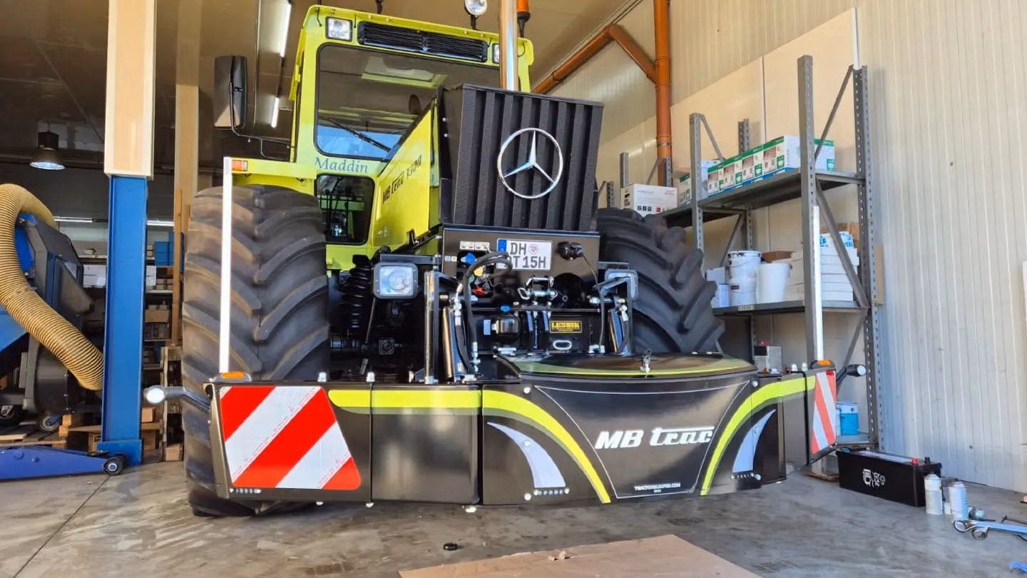 Large tractor indoors with a black front weight bumper featuring reflectors and MB trac lettering