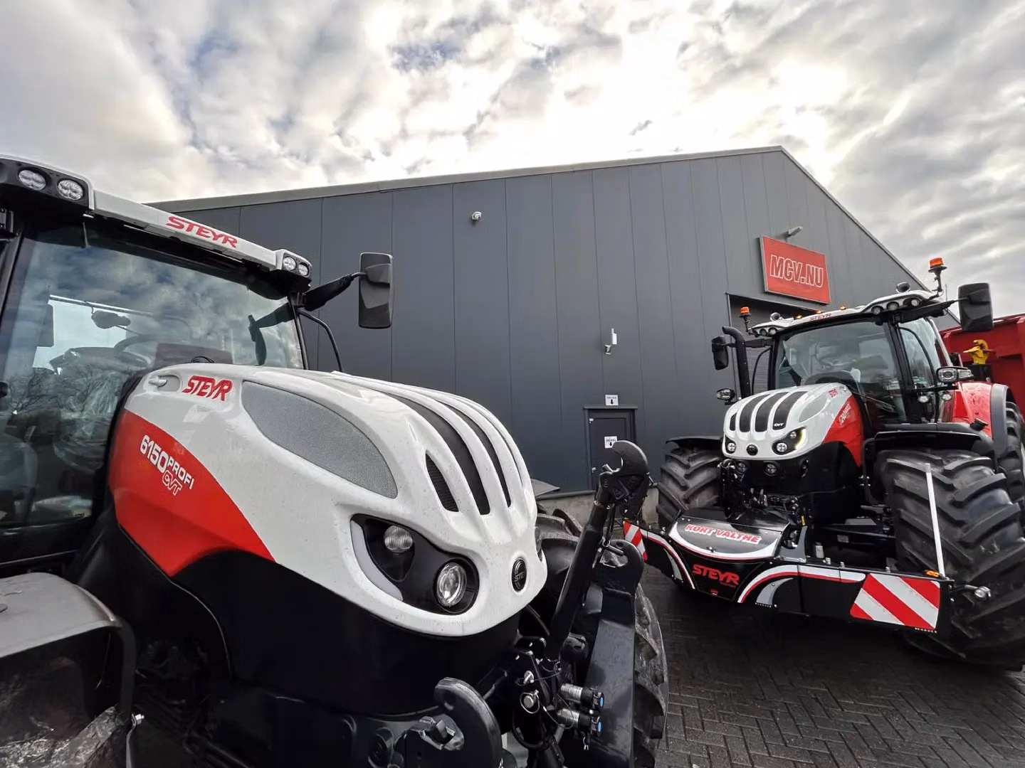 Two Steyr tractors parked outside a building, the nearer one fitted with a front weight bumper featuring LED lighting