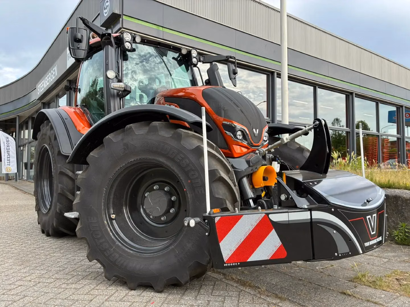 Large red tractor with a black front weight bumper featuring reflective stripes and integrated LED lights