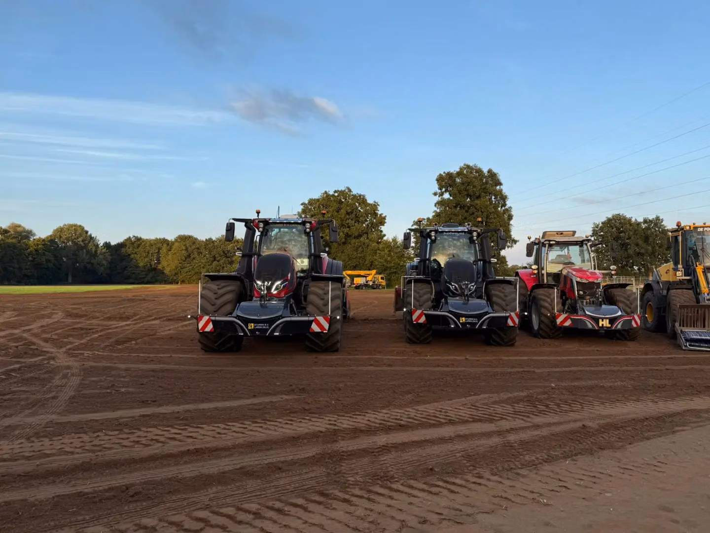 Three tractors with front weight bumpers featuring LED lights and reflective stripes are parked on a dirt field