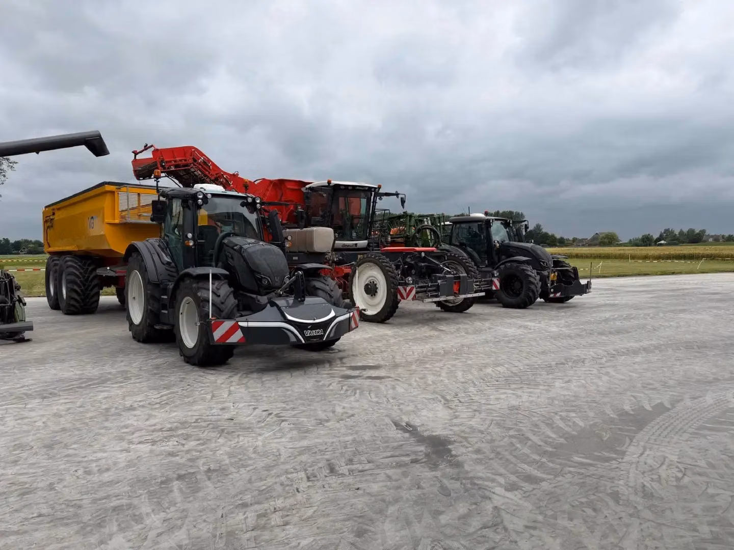 Three tractors equipped with front weight bumpers are parked on a concrete surface next to farm equipment