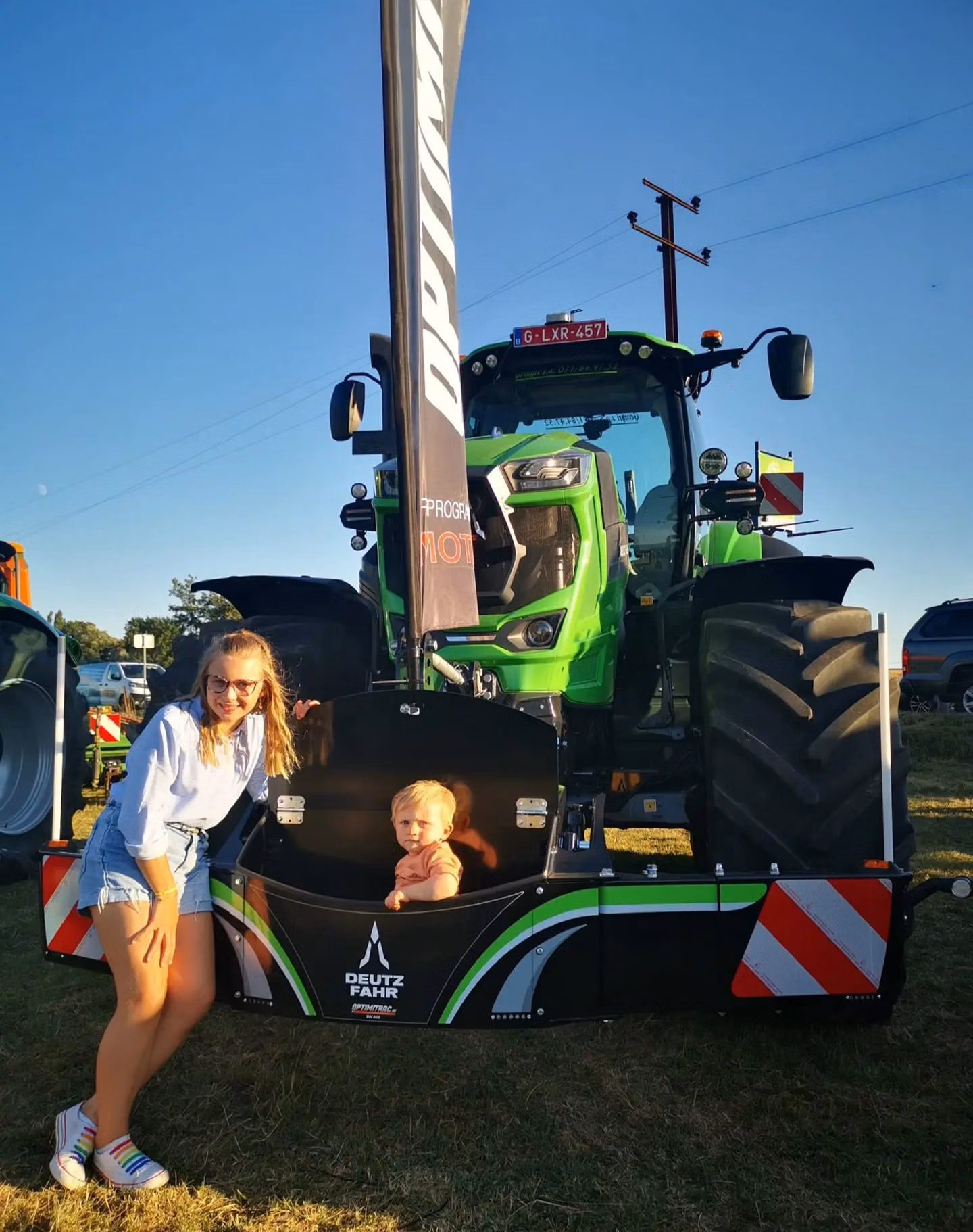 A woman and a child stand by a Deutz-Fahr front weight bumper attached to a green tractor outdoors