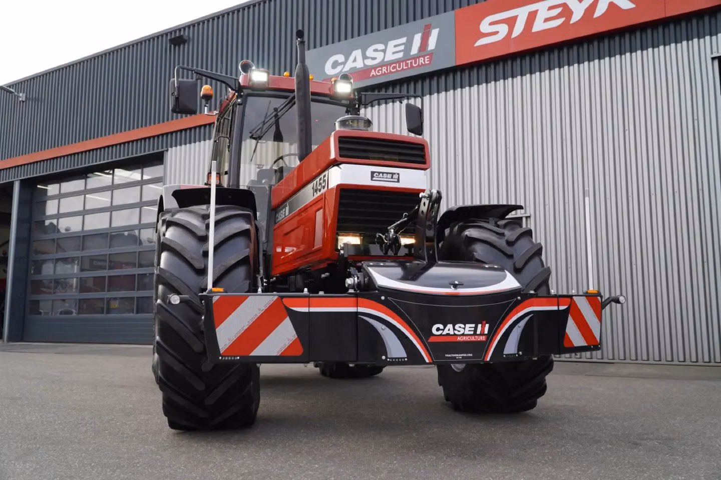 Red Case IH tractor with large tires and a black front weight bumper featuring red and white reflective stripes