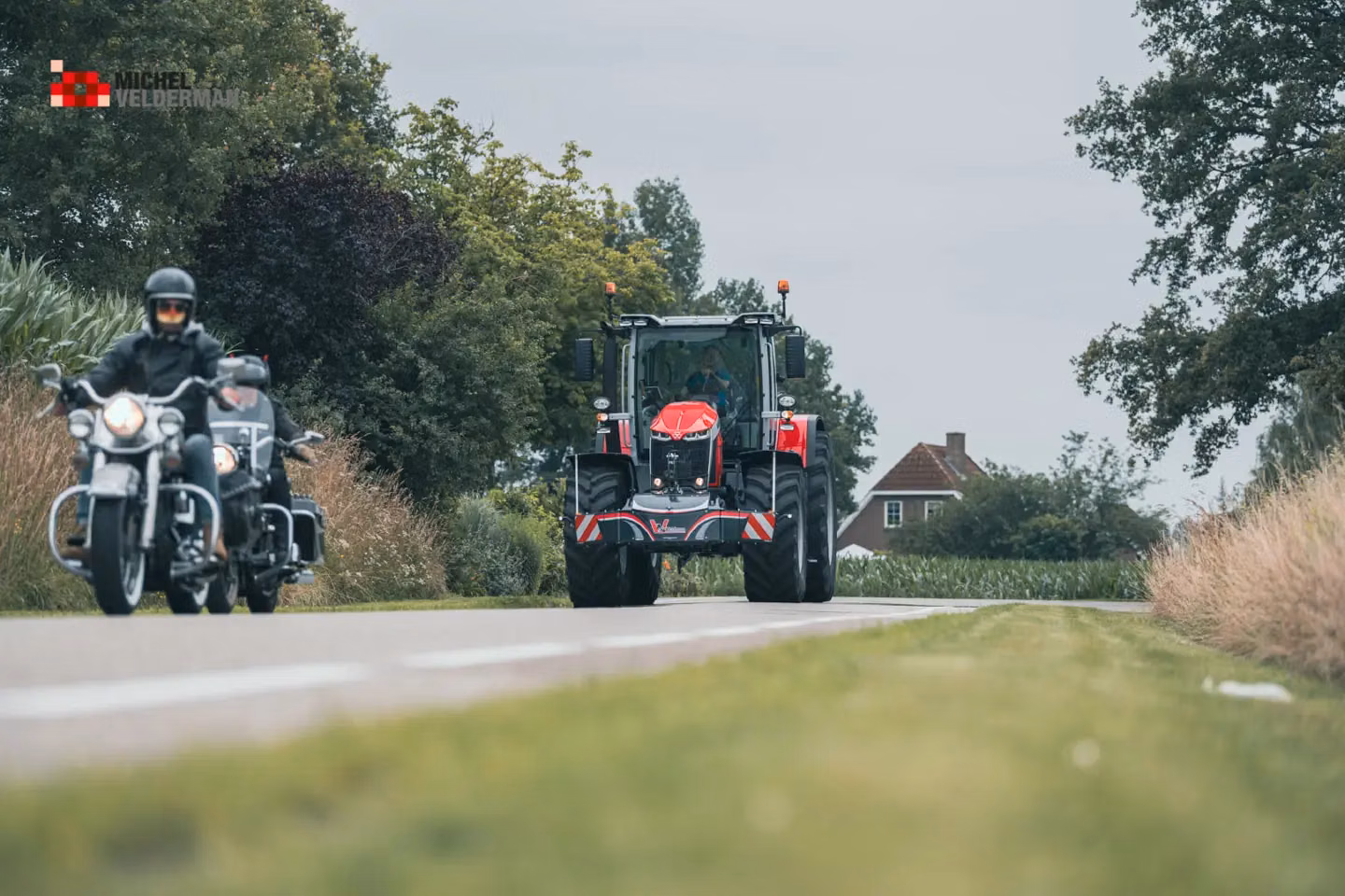 Red tractor with a front weight bumper drives on a rural road as two motorcyclists pass in the opposite direction