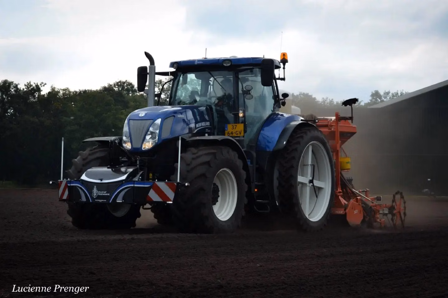Blue tractor with a front weight bumper and rear-mounted implement working on a dirt field