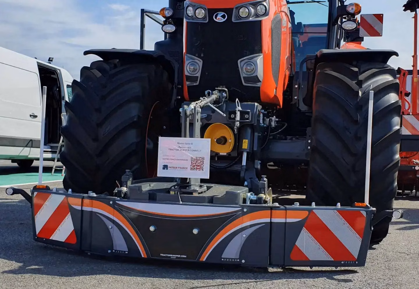 Large orange tractor with a mounted front weight bumper featuring reflective red and white diagonal stripes