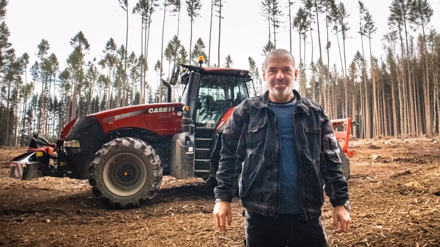 Man standing in front of a Case IH tractor with a front weight bumper in a forest clearing