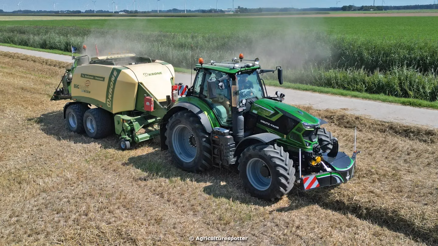Green tractor with a front weight bumper pulling a yellow baler on a harvested field next to a rural road
