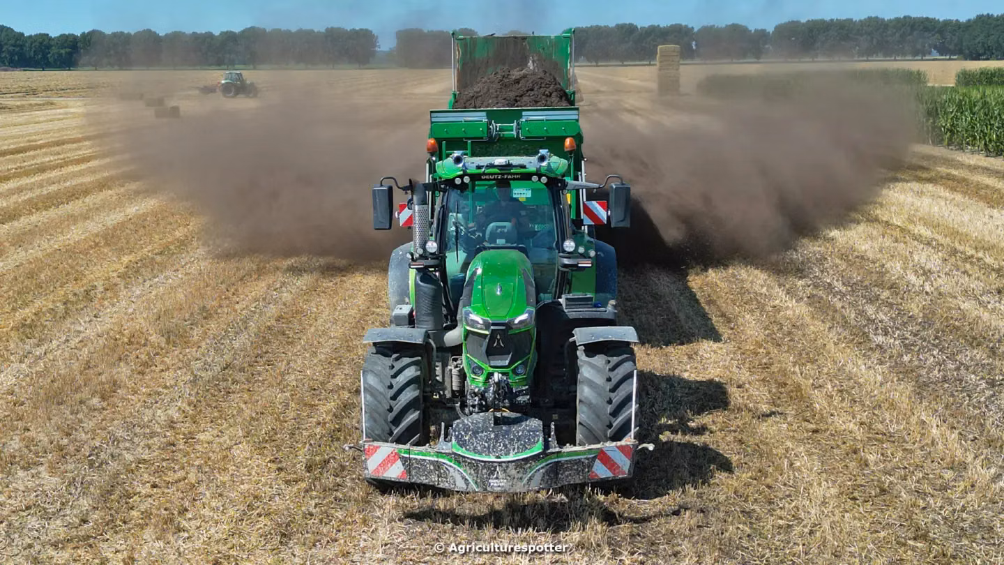 Green tractor in a field with a front weight bumper, spreading soil from a rear attachment