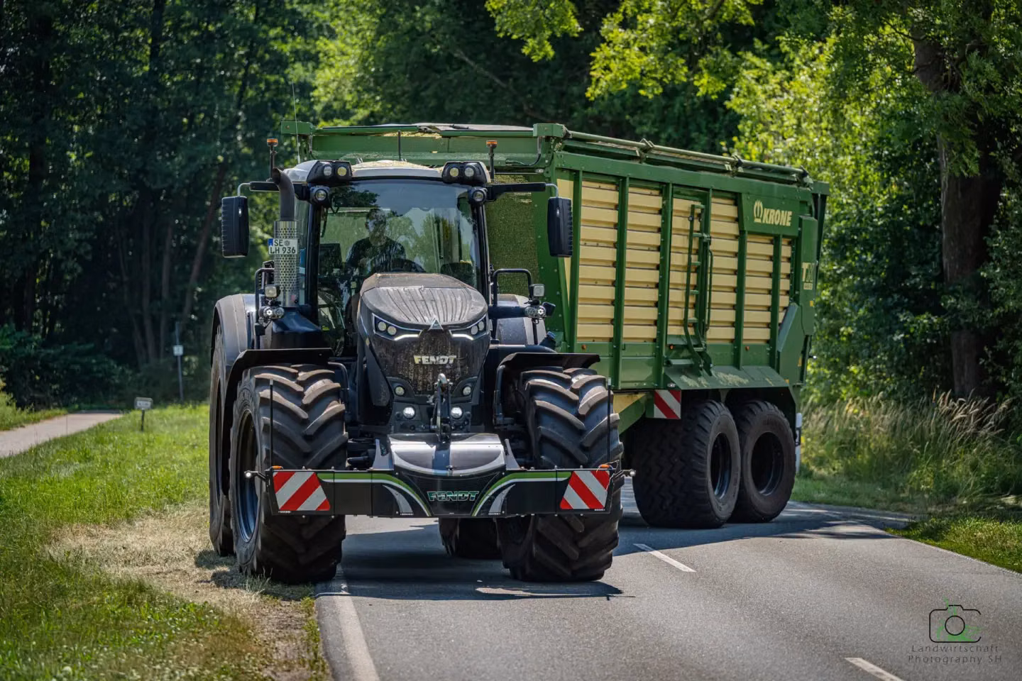 A tractor with a front weight bumper and warning markings is pulling a large green trailer on a rural road