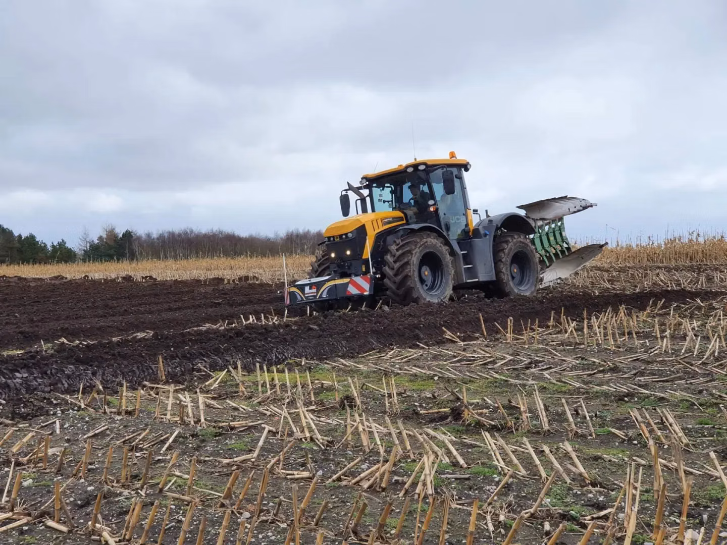 A yellow and black tractor with a front weight bumper and rear plow works in a freshly tilled field