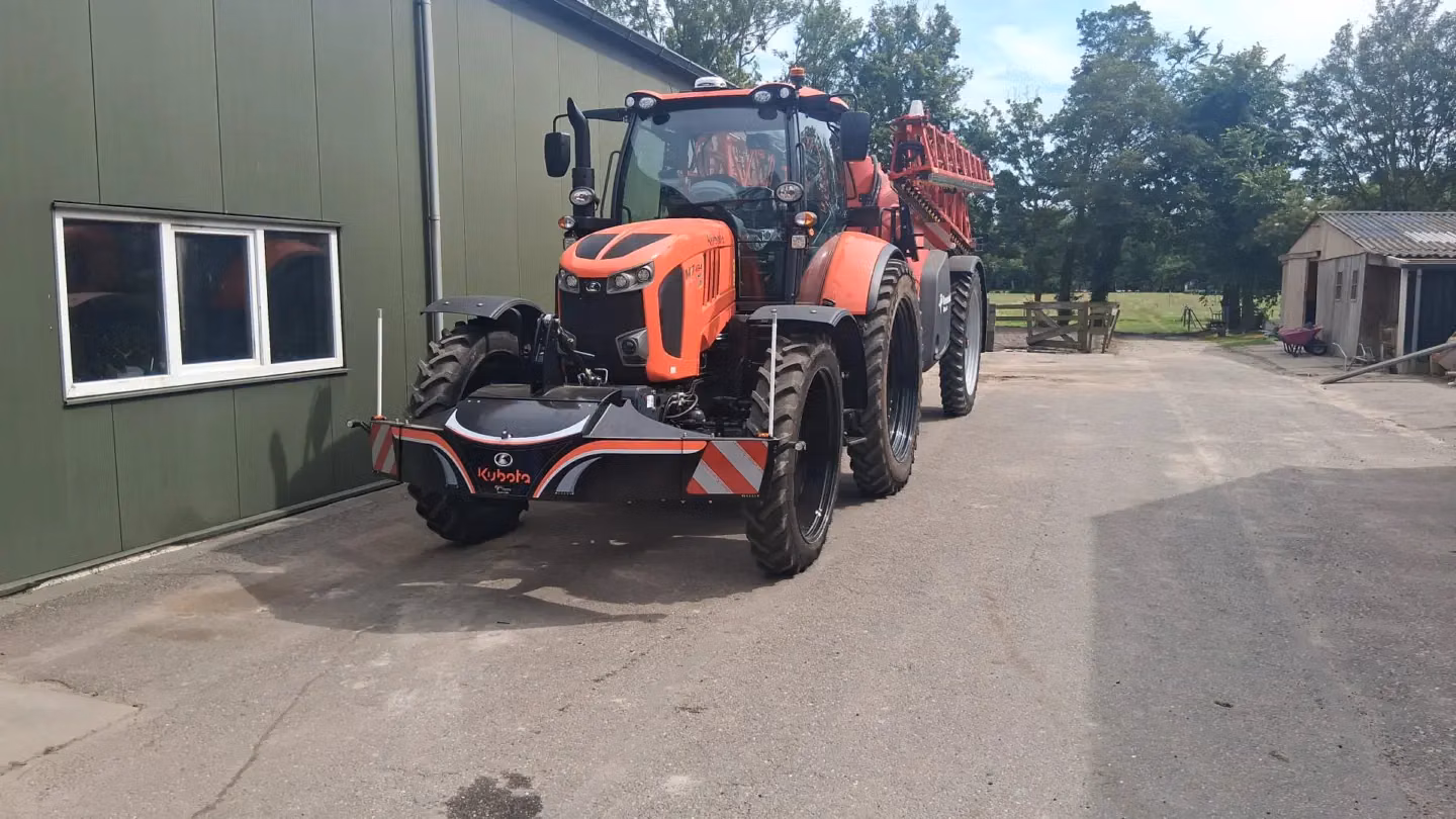 Orange tractor with a large front weight bumper featuring red and white reflective stripes on a farm driveway