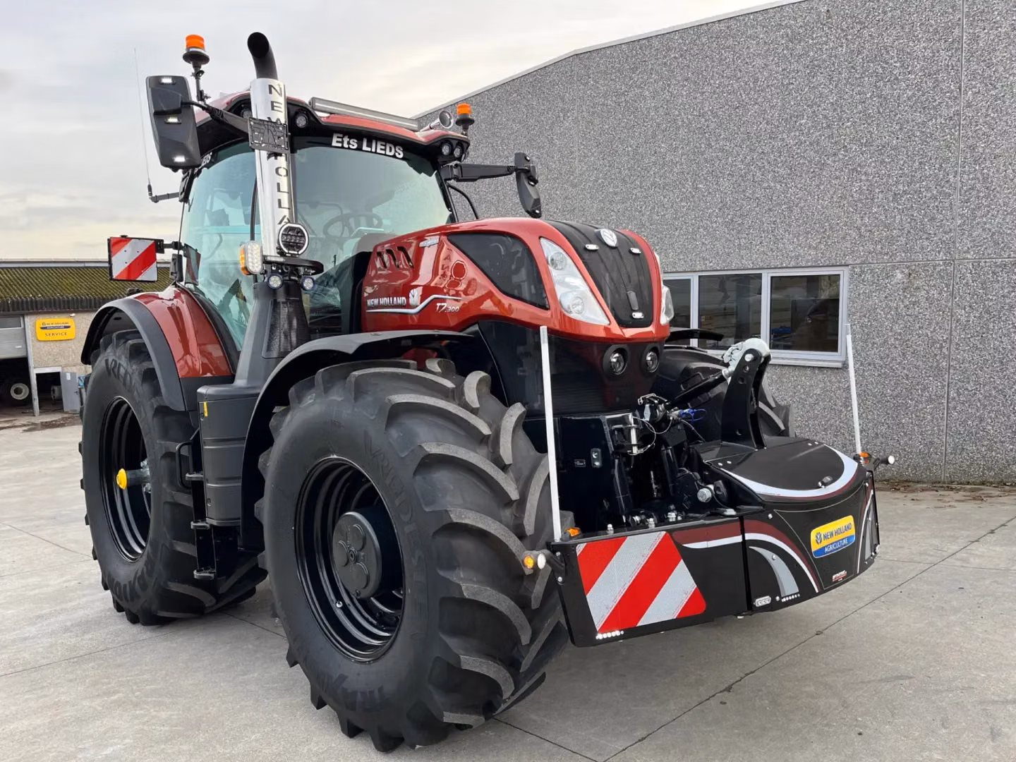 A red tractor with a large front weight bumper featuring red and white stripes and a New Holland Accessories sticker
