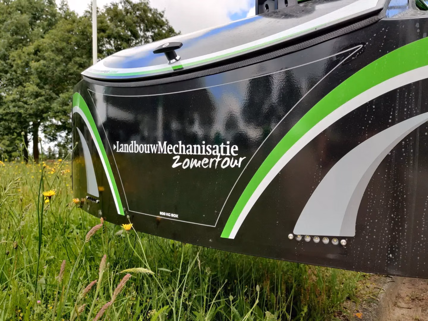 Close-up of a black front weight bumper with green and grey accents, LED lights, and text in a grassy field