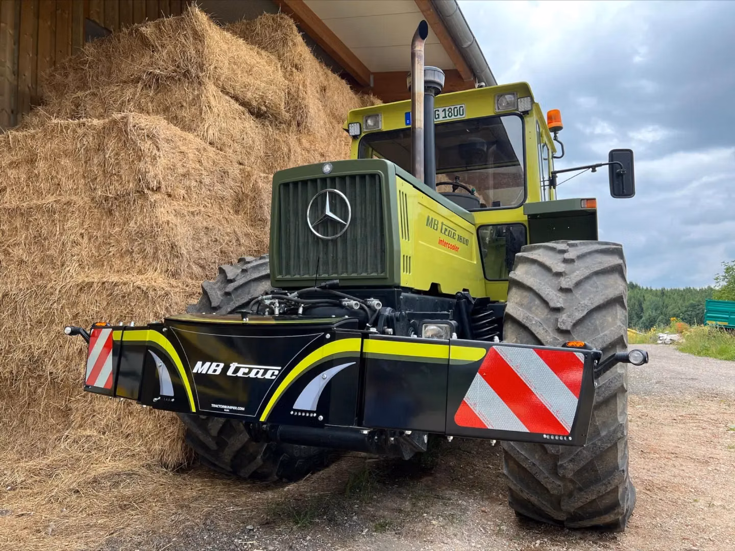 A green tractor with large tires is fitted with a front weight bumper featuring reflective red and white stripes