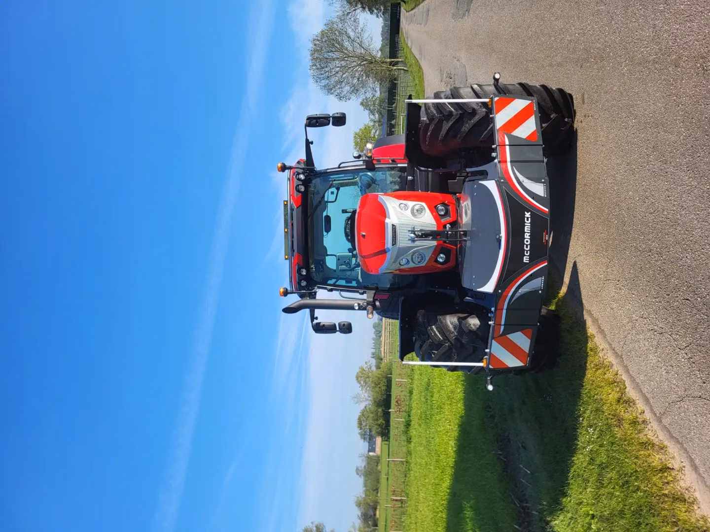 Red tractor with a McCormick front weight bumper featuring LED lights and safety markings parked on a rural road